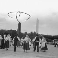 Then: Yugoslav dancers rehearse on the South Terrace of the National Museum of History and Technology, now the National Museum of American History, before their performance at the seventh annual Festival of American Folklife, June 30 - July 8, 1973. Behind the dancers is the sculpture "Infinity." The Washington Monument can be seen in the distance. (Photo by Harry B. Neufeld, Smithsonian Institution)