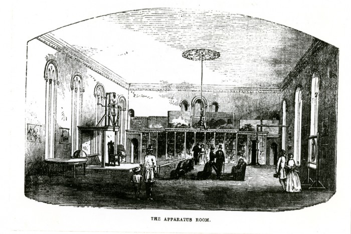 Print of an engraving of the Apparatus Room of the Smithsonian Institution Building, or "Castle," with the electrical machines constructed by Dr. Robert Hare, a professor of chemistry at the University of Pennsylvania. Dr. Hare donated his collection of chemical and physical apparatus to the Institution in 1848. Men and women are talking and walking around. The engraving was published in the Smithsonian Guidebook of 1857