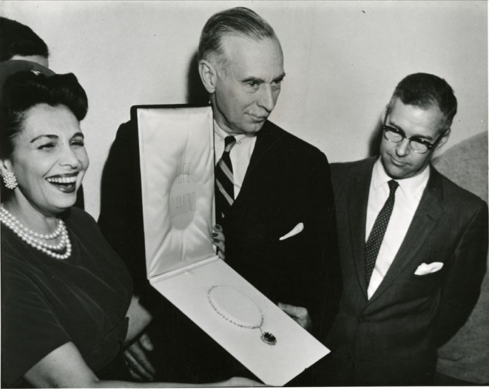 A woman and two men holding jewel case with necklace.