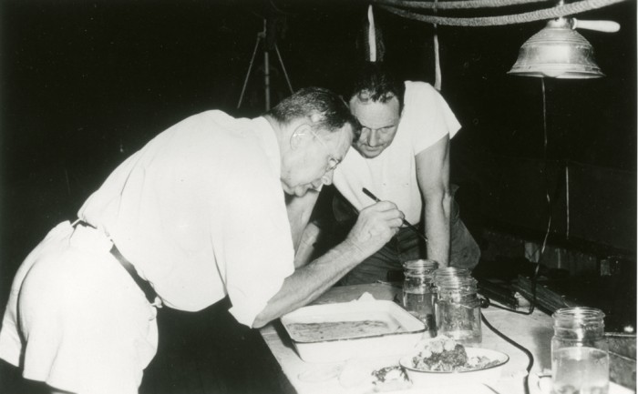 On board the ship "Freelance", J. F. Gates (John Frederick Gates) Clarke, 1905-1990, left, and Waldo LaSalle Schmitt, 1887-1977, right, part of the Smithsonian-Bredin Caribbean Expedition of 1956, examine specimens they collected. . F. Gates (John Frederick Gates) Clarke, 1954-1963, was curator of Lepidoptera and Waldo LaSalle Schmitt, 1957-1977, was curator of Invertebrate Zoology, at the National Museum of National History