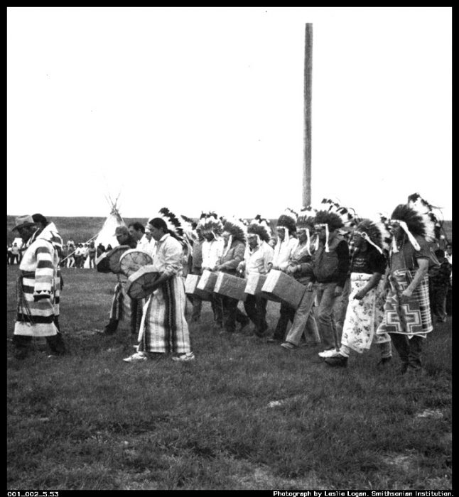 Indians in tribal dress carry boxes of remains