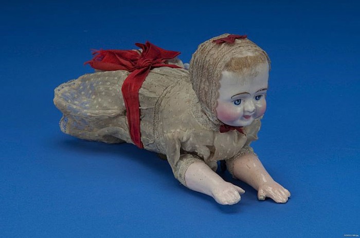 This doll, made c. 1900, was an improvement on Clarke's design. Inside the doll's body is a spring-driven brass mechanical movement that actuates the arms and legs in imitation of crawling, though the doll actually moves along on two concealed wheels.