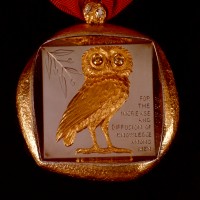 The Smithsonian’s Badge of Office is a thick, irregularly shaped medallion made of 18-carat gold that hangs from a cherry-red ribbon. Cast in high relief and set within a deeply recessed square on the front is the owl of Athena, a symbol of wisdom, and an olive branch, a symbol of peace and goodwill. The owl has forward-gazing eyes that are set with a pair of large, yellow sapphires. To the side of the owl is engraved the Smithsonian Institution’s mandate as defined in James Smithson’s will: “For the Increase and Diffusion of Knowledge Among Men.” The back is engraved with the sunburst seal of the Smithsonian and “James Smithson, 1765—Bicentennial 1965.” (Image courtesy Smithsonian Institution)