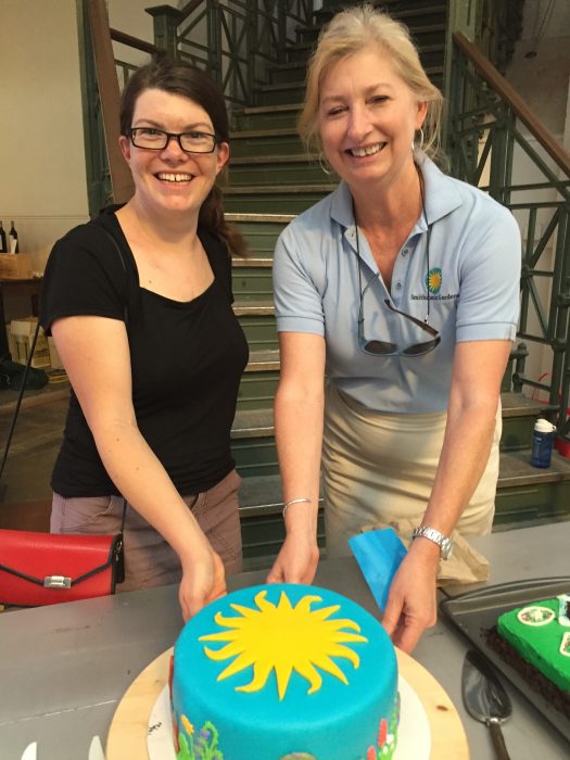 Smiling women with cake decorated with blue and yellow Smithsonian logo.