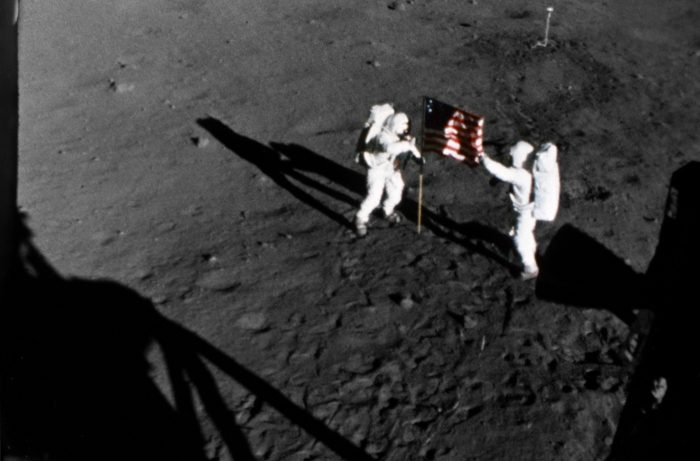 Astronauts with flag in the shadow of the lunar module
