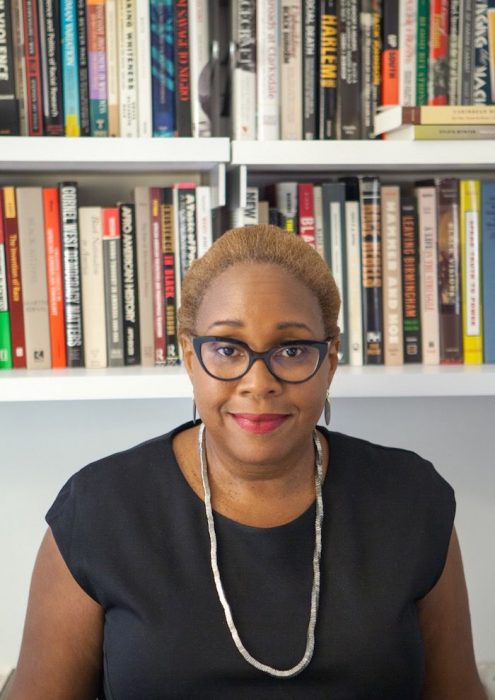 Portrait of Wilson wearing black dress and glasses, bookshelves behind her