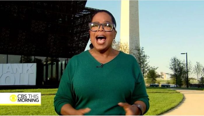 Winfrey in green sweater and glasses in front of museum