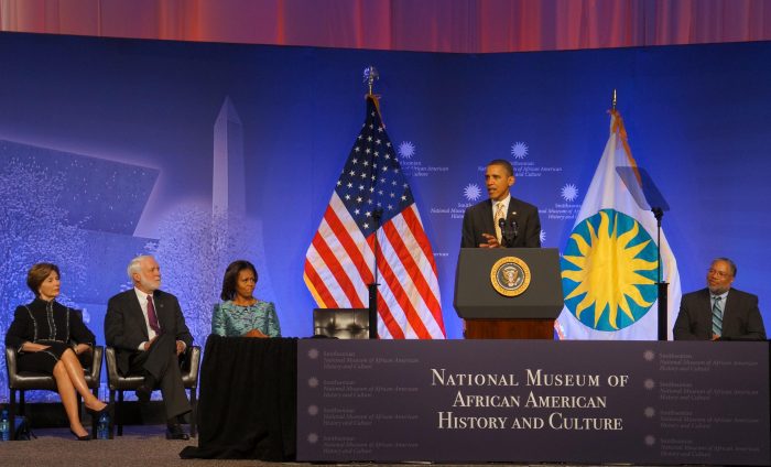 President Obama at podium, American and Smithsonian flags in the background