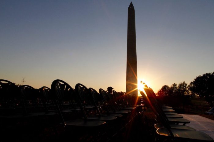 Sun sets behind Washington monument, one person sitting in row of empty chairs