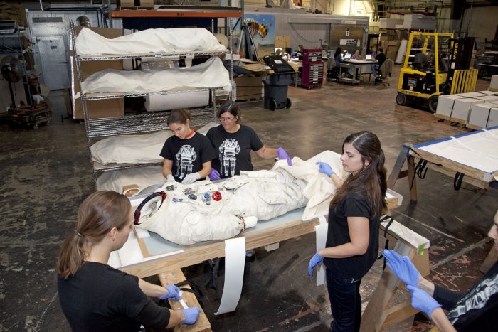 Conservators grouped aroubnd spacesuit on table