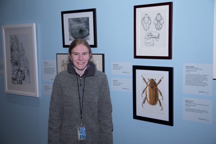 Artists standing with her work in exhibition gallery