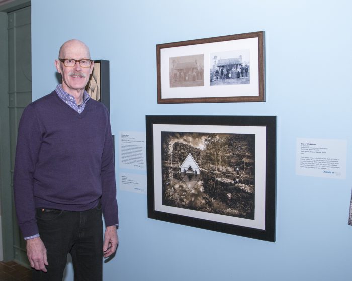 Artist stands next to his work in exhibition gallery