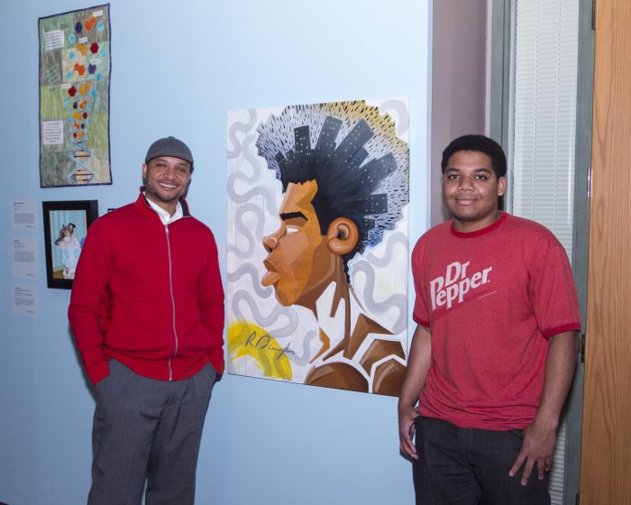 Artist and young man stand next to painting in exhibition gallery 