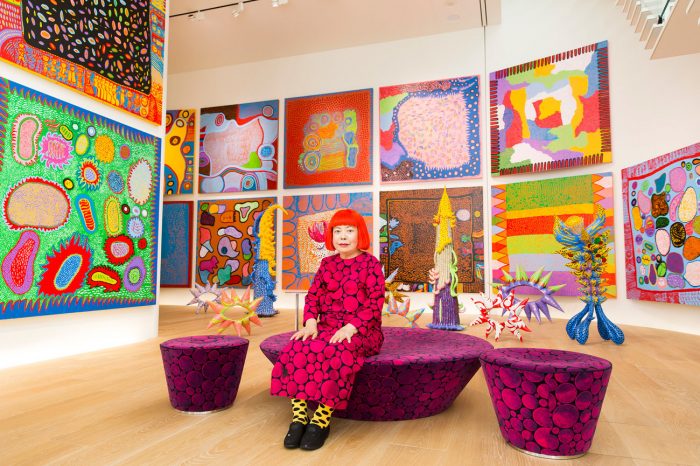 Artist in colorful dress and wig ingallery of bright paintings