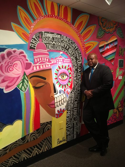 Man in suit leans against colorful mural wall