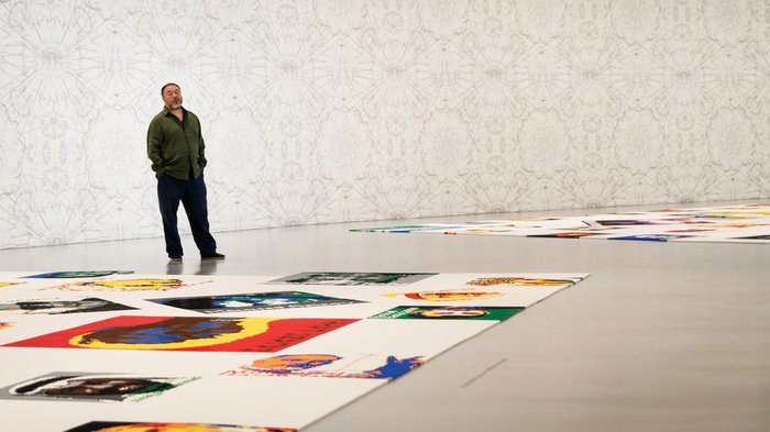 Ai Weiwei in gallery with portraits on floor