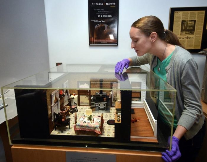 Woman peers into case of dollhouse furniture