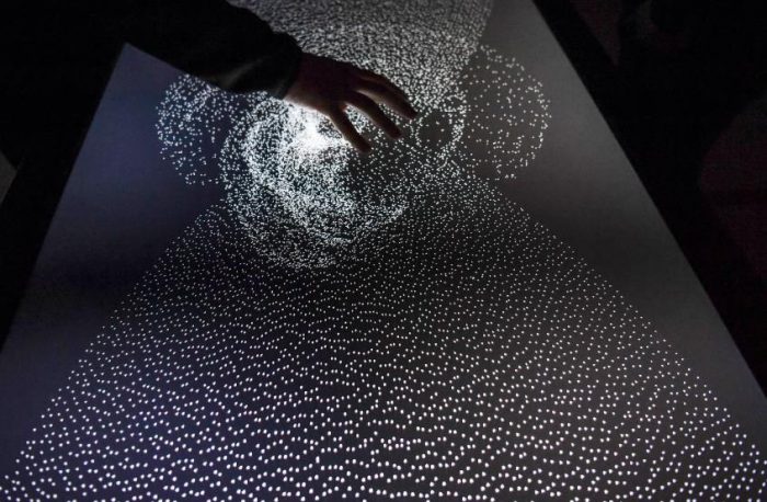 Hand on interactive screen showing white dots