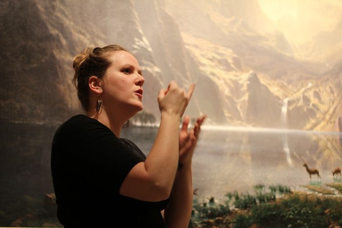 Woman discusses large landscape painting in ASL
