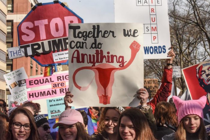 Women hold signs protesting Trump