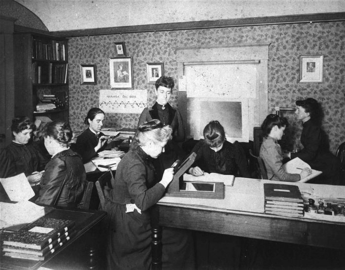 Women making calculations in crowded workroom