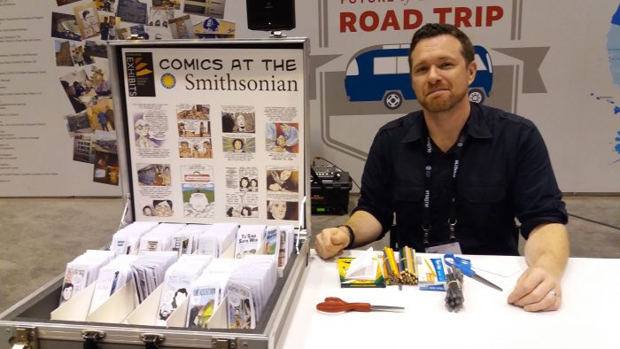 Evan Keeling at desk with display case Comics at the Smithsonian