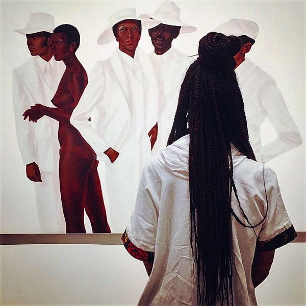 Black woman in gallery looks at painting of African American people