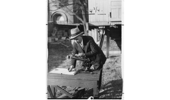 Man in suit and hat bending over a scientific instrument