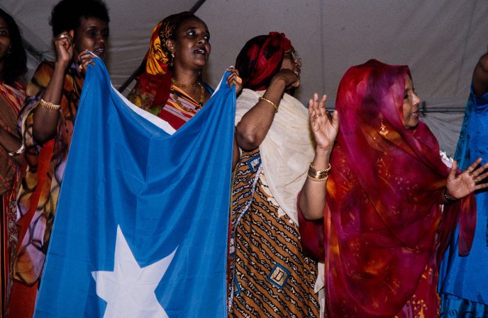 Women clapping and singing, one holding flag