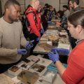 Two people wearing gloves at table of artifacts