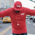 DJ in red hat and shirt holding arms outstretched on city street