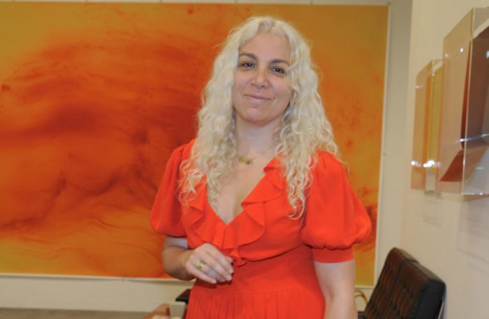 Rosen in bright orange dress stands in front of orange painting