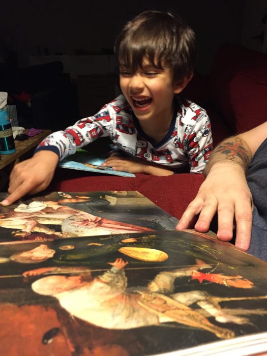 Young boy laughing and pointing at art book