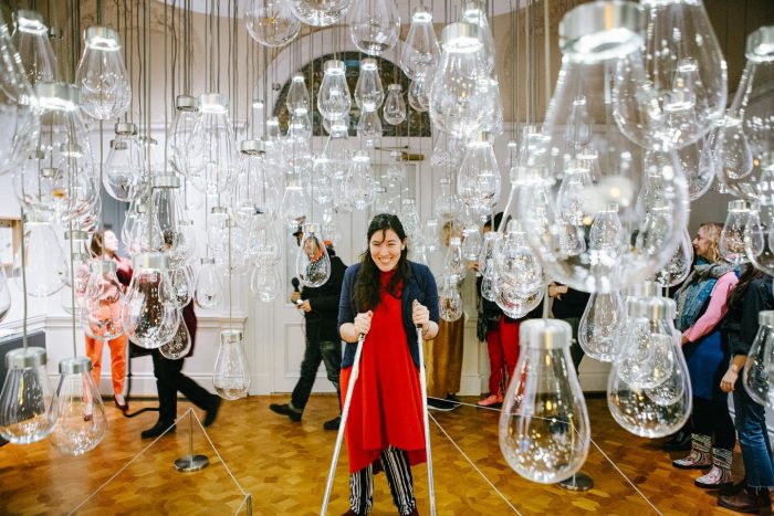 Woman in red dress with crutches surrounded by suspended glass bulbs