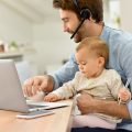 man works at laptop while holding baby