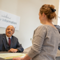 Volunteer at infomration desk talks to woman with her back to camera