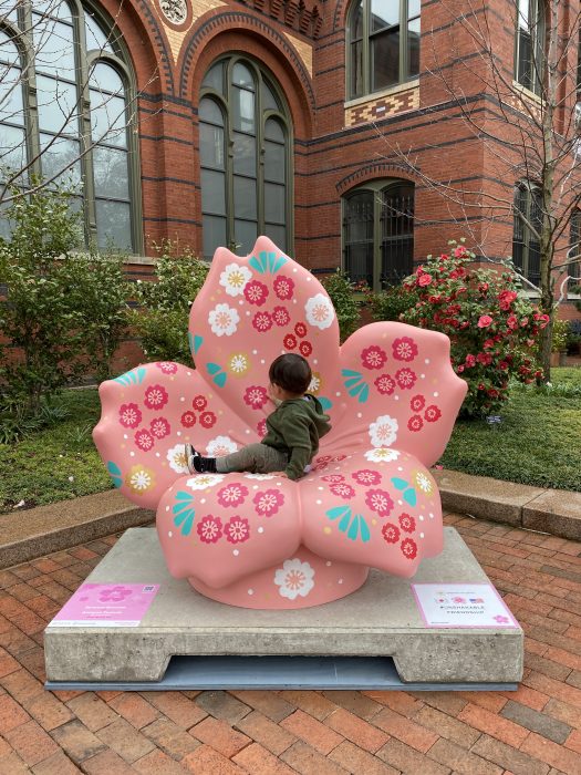 Young child (back to camera) sitting on Renewal Blossom sculpture