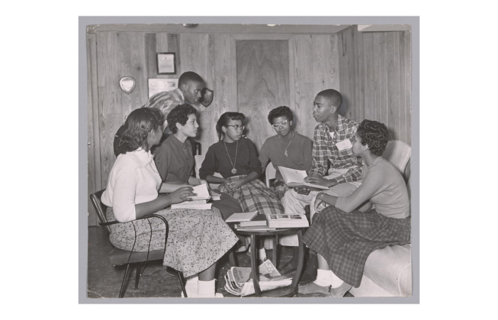 Black and white photo of several young Black people gathered around ata\ble