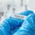Stock photo of blue-gloved hand holding syringe with "Covid-19 Vaccine"