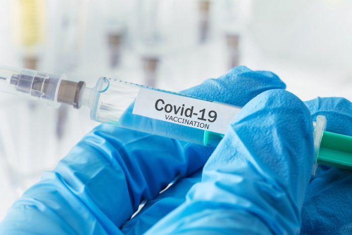 Stock photo of blue-gloved hand holding syringe with "Covid-19 Vaccine"