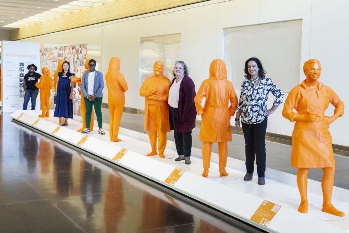 women pose next to their statues