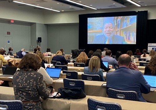 Secretary Bunch is seen on large video screen in front of conference attendees