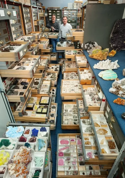 two_smithsonian_staff_stand_in_an_aisle_of_the_mineral_sciences_collection_storage_room_the_drawers_are_pulled_out_to_show_the_colorful_minerals_within