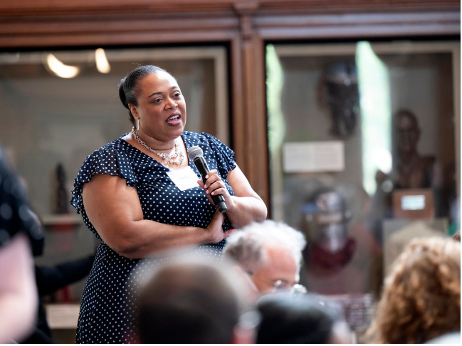 Chism, in polka-dot dress, holds mic and addresses teachers in the Smithsonian Castle's Commons.