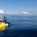 Small one-person submersible on surface of ocean, blue sky and clouds in background
