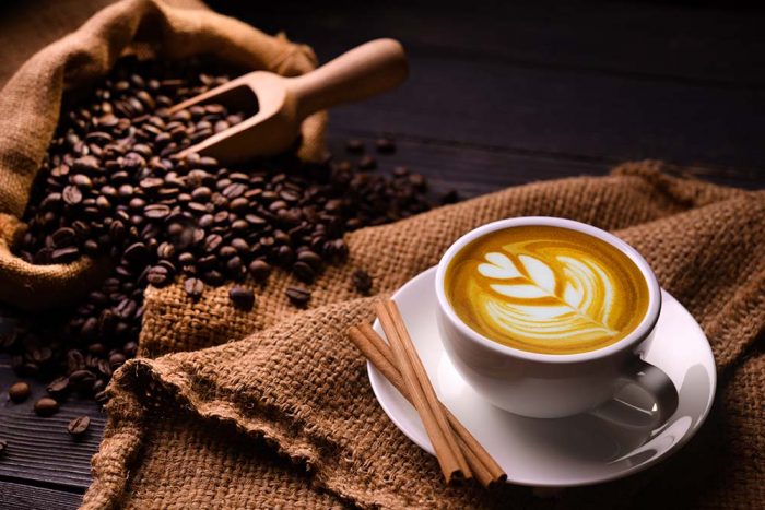 Cup of coffee latte and coffee beans in burlap sack on old wooden background