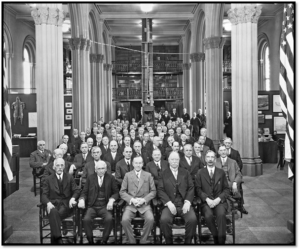 1927 black and white photo of Secretary Walcott and Smithsonian staff and regents seated on chairs in the Great Hall of the Smithsonian Institution Building