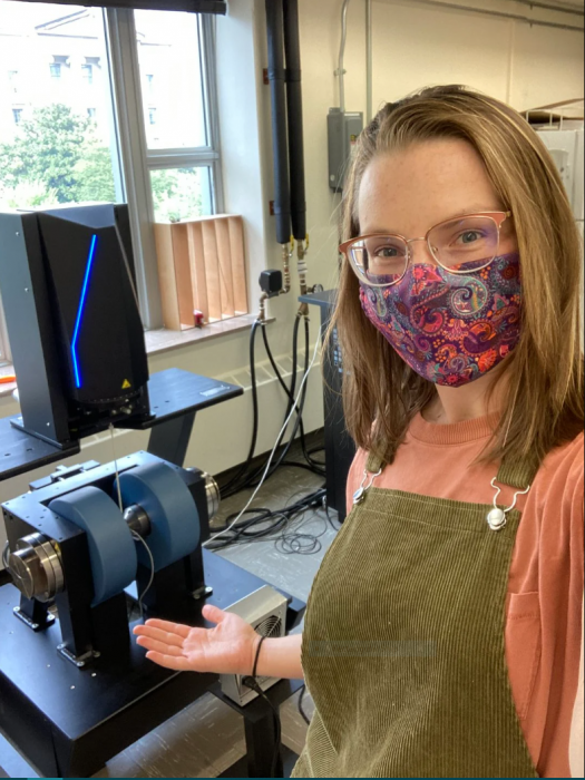 Courtney Wagner, wearing paisley face mask, gestires at micrscope in lab