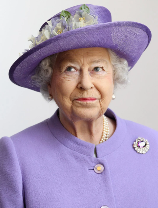 Queen ELizabeth in purple hat and suit smiling impishly