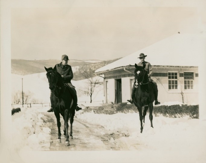 Two cavalry officers on horseback in front of stucco building